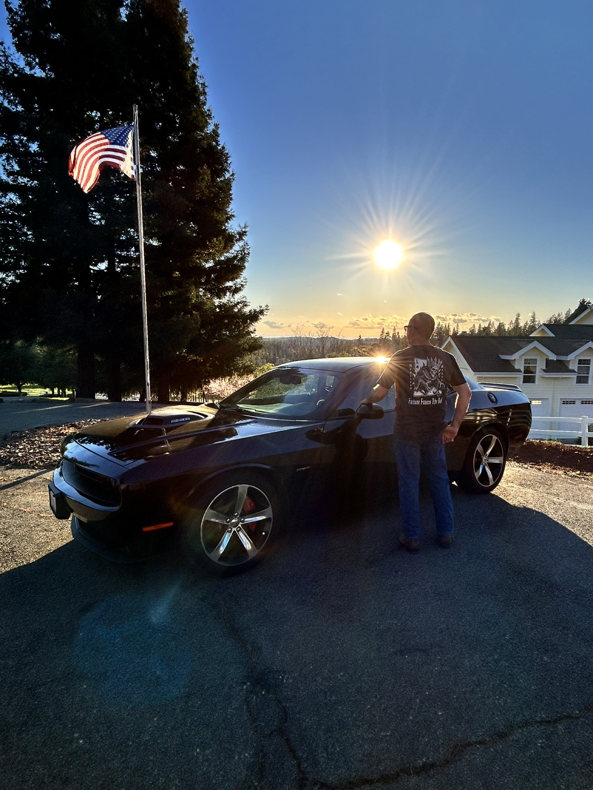 Man with Dodge Challenger and American flag at sunset